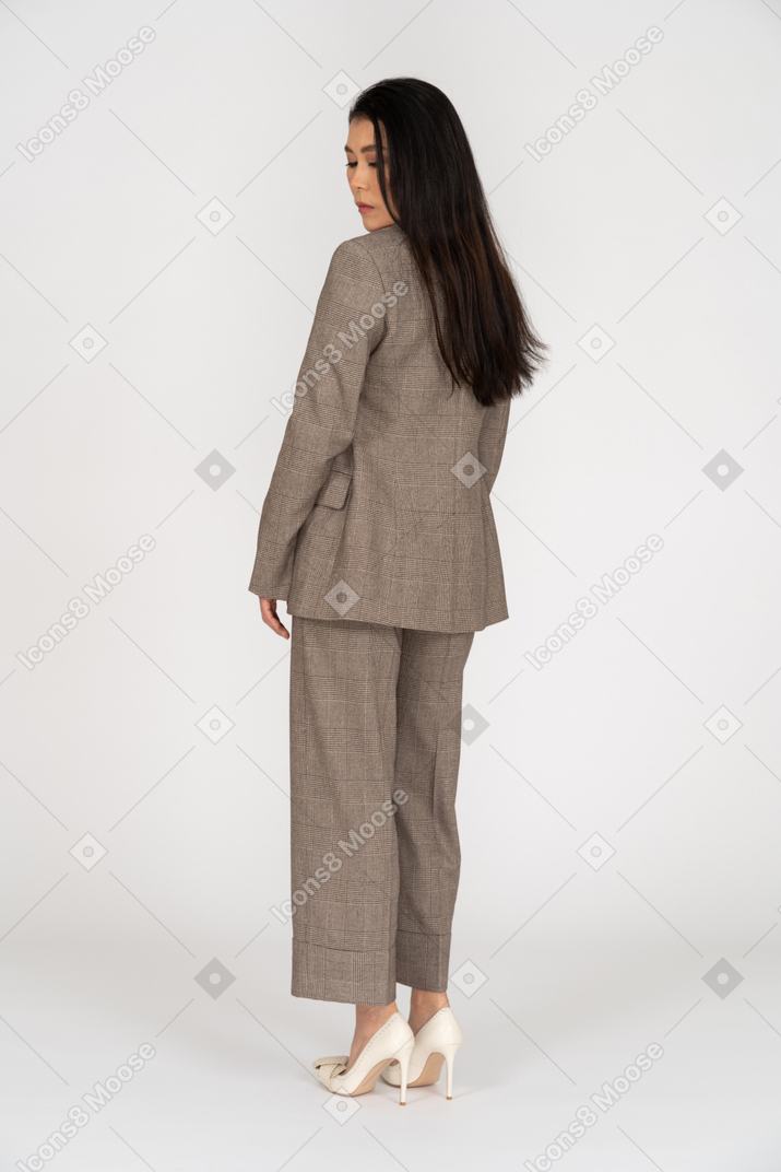 Three-quarter back view of a young lady in brown business suit looking down