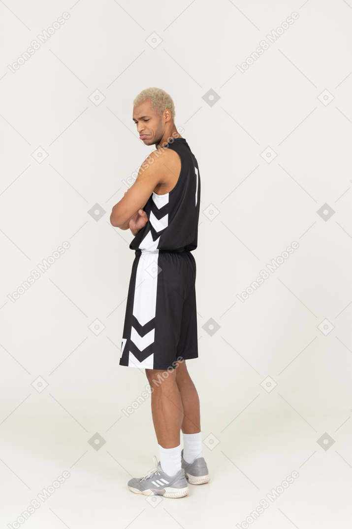 Three-quarter back view of a withdrawn young male basketball player crossing arms
