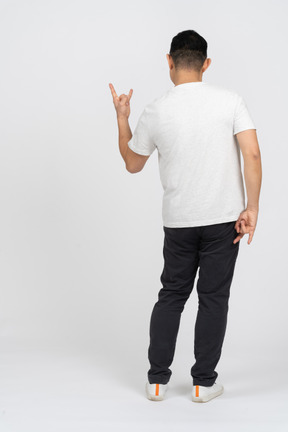 Homem em roupas casuais em pé de costas para a câmera e mostrando o gesto de rock