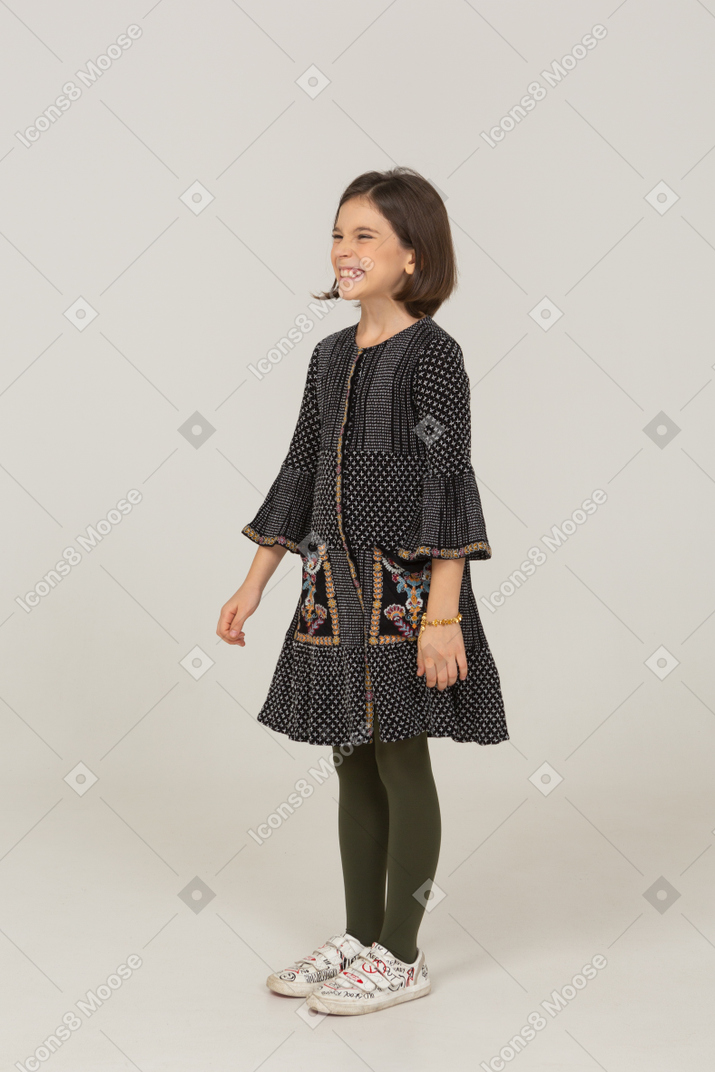 Vista di tre quarti di una bambina sorridente che fa una smorfia in abito