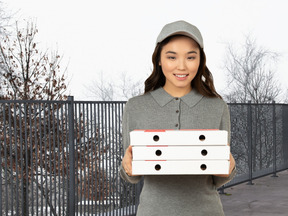 A delivery woman holding pizza boxes in front of a fence