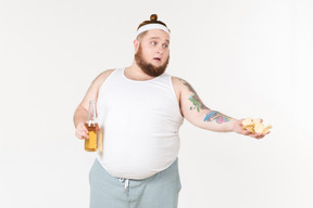 Um homem gordo em sportswear segurando uma garrafa de cerveja e oferecendo chips