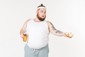 A fat man in sportswear holding a bottle of beer and offering chips