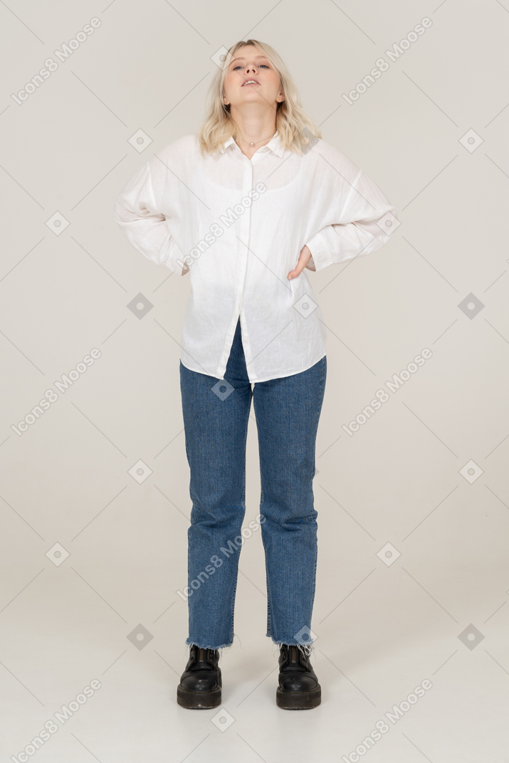 Front view of a blonde female in casual clothes putting hands on hips and looking up