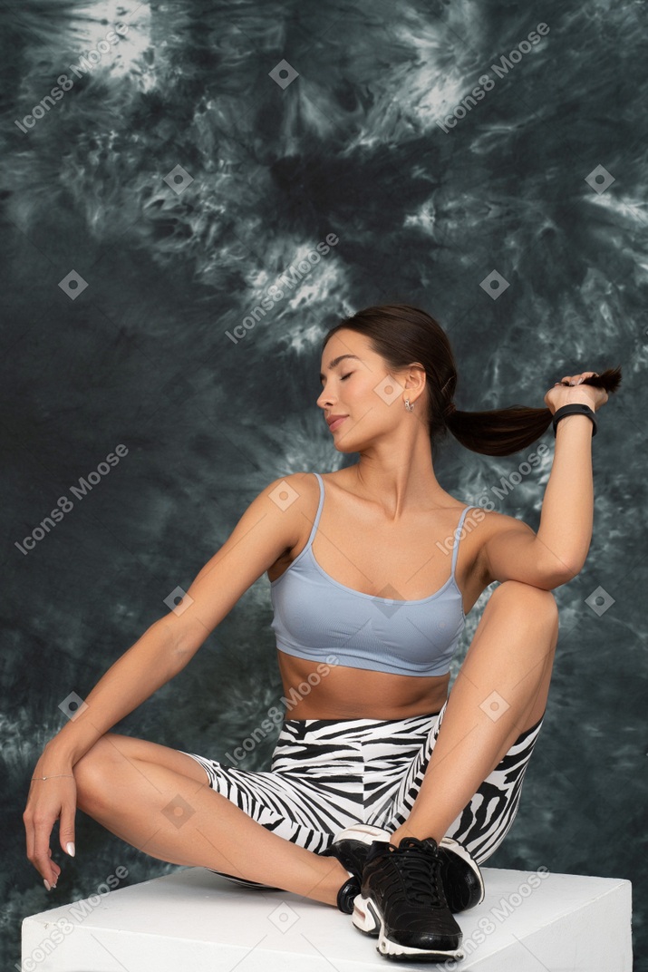 A female athlete sitting on a cube touches her long hair