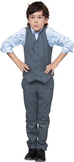 Vue de face d'un garçon en costume posant avec les mains sur les hanches