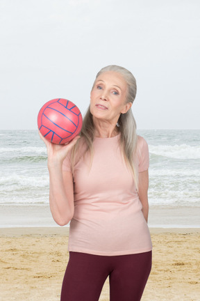 An older woman holding a ball on the beach