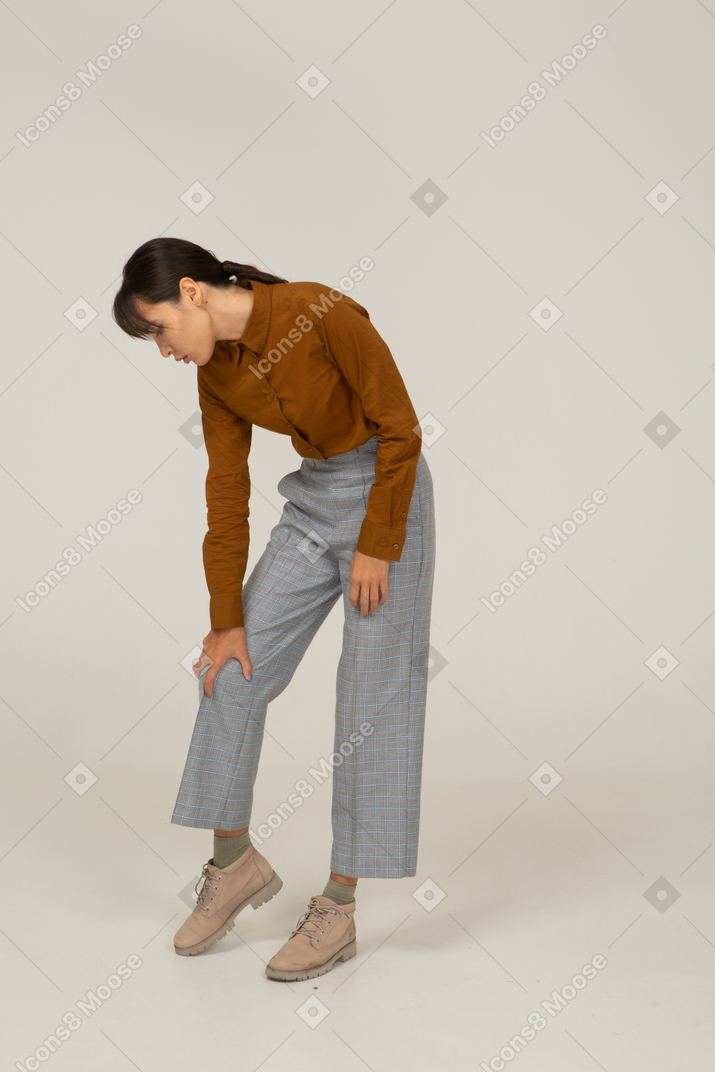 Vista frontal de uma jovem mulher asiática de calça e blusa, inclinada para a frente