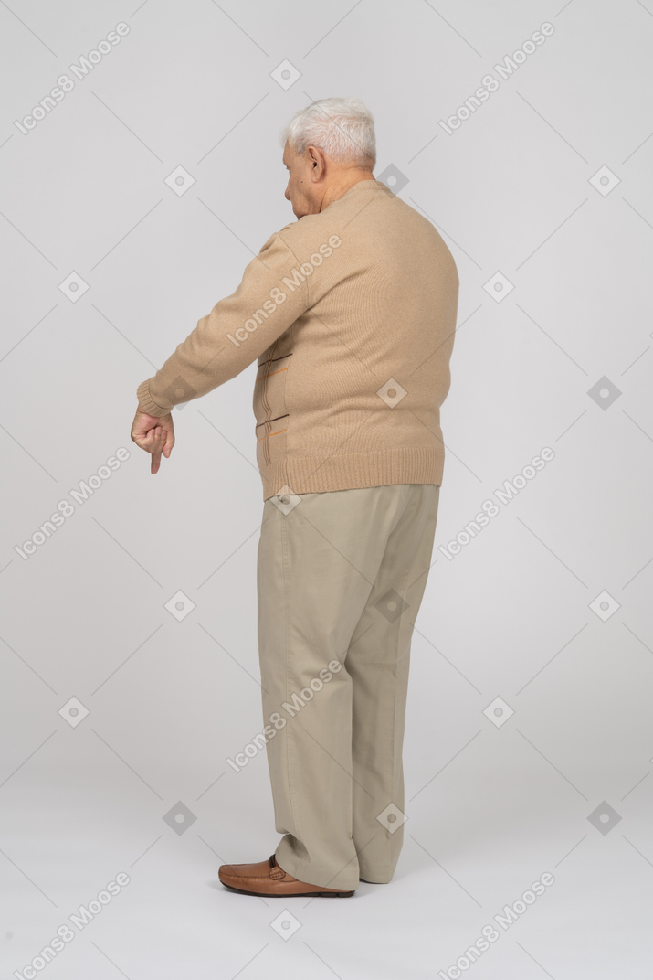 Side view of an old man in casual clothes pointing down with a finger