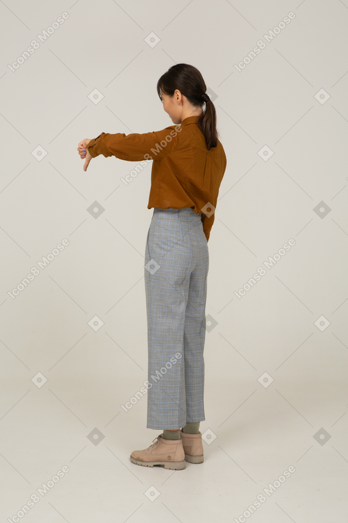 Vista de tres cuartos de una joven mujer asiática en calzones y blusa mostrando el pulgar hacia abajo