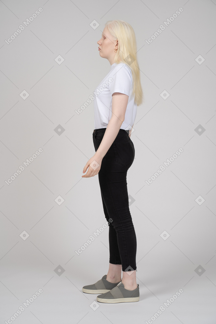 Вид сбоку на молодую женщину в повседневной одежде, стоящую и смотрящую в сторону