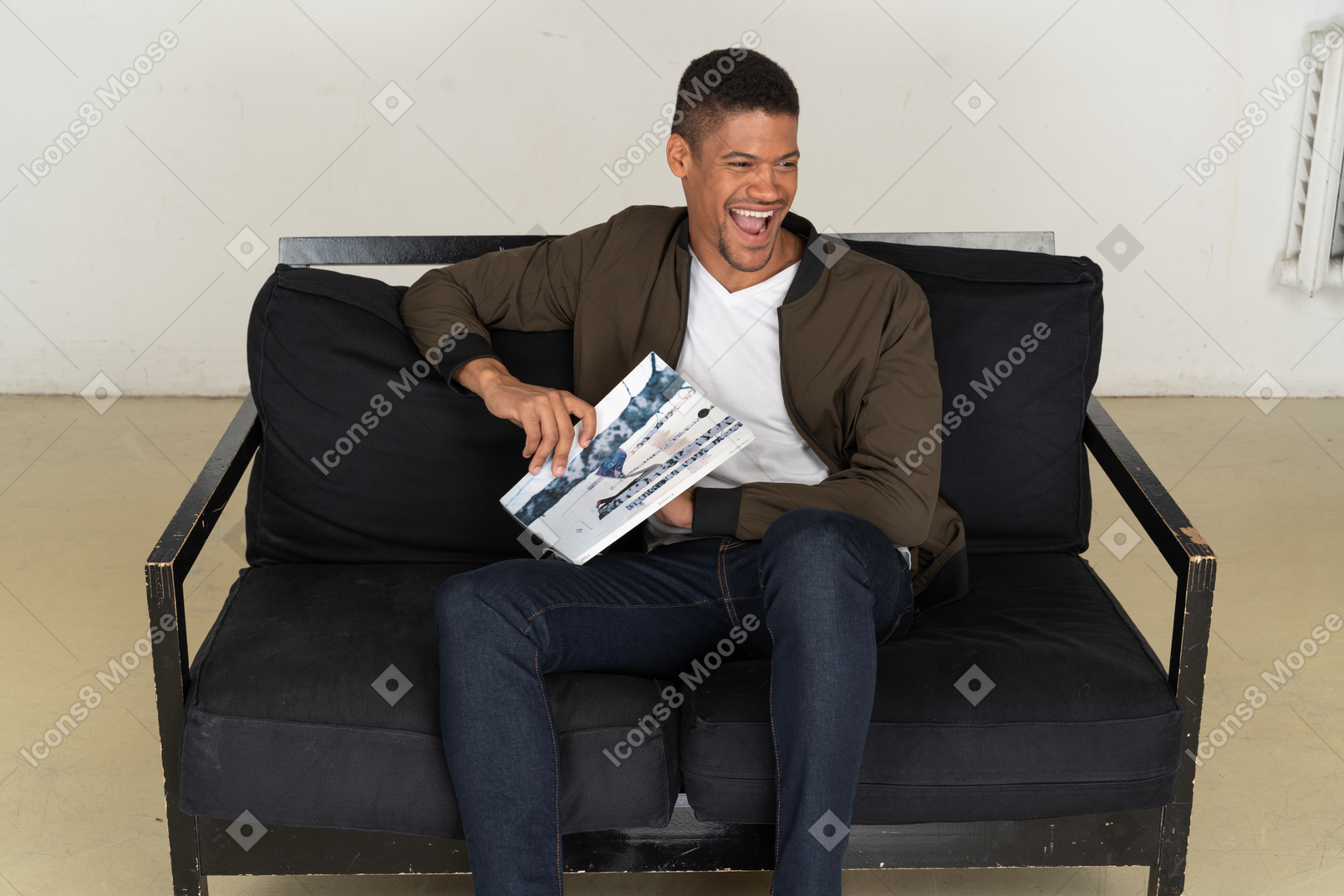 Beautiful young man sitting on a sofa and holding a magazine