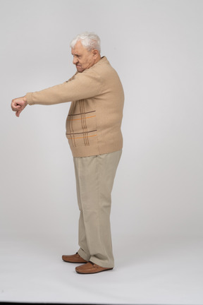 Vista lateral de un anciano con ropa informal que muestra el pulgar hacia abajo