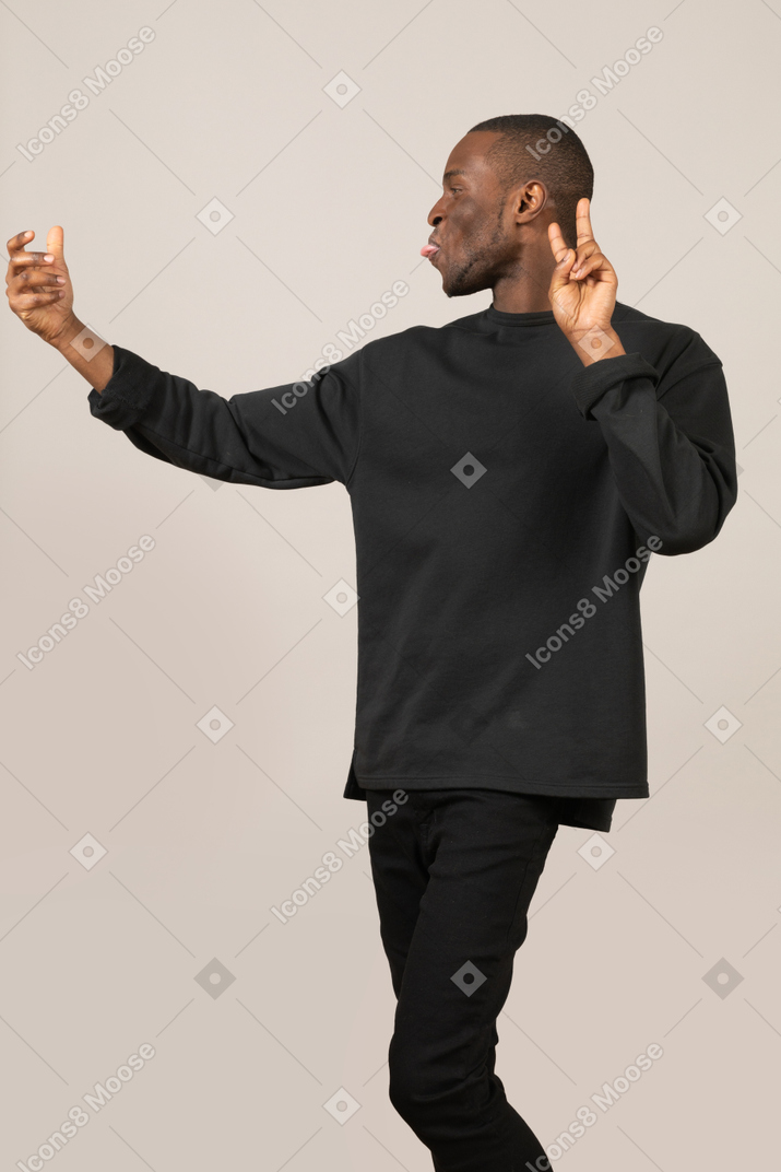 Side view of man taking selfie with imaginary smartphone and showing tongue