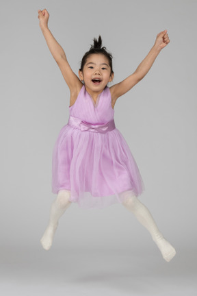 Niña feliz en un vestido rosa saltando con los brazos y las piernas abiertas