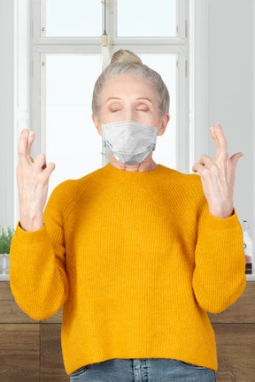 An older woman with face mask standing with fingers crossed