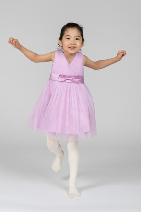 Girl in a pink dress jumping on one leg