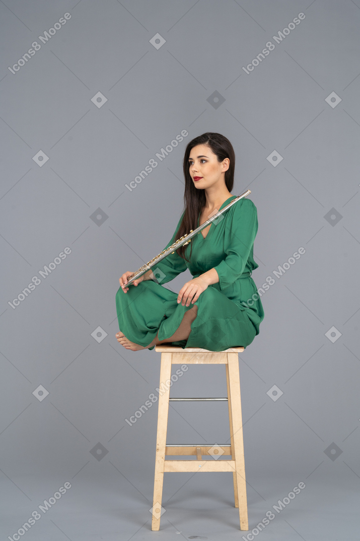 Comprimento total de uma jovem segurando o clarinete, sentada com as pernas cruzadas em uma cadeira de madeira