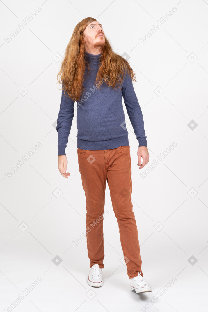 Vista frontal de un joven con ropa informal caminando y mirando hacia arriba