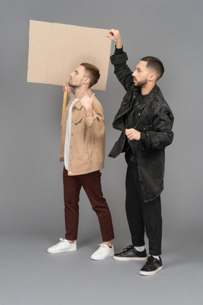 Side view of two young men with a raised billboard looking slightly agitated