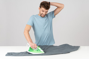 Young handsome guy ironing shirt and looking worried