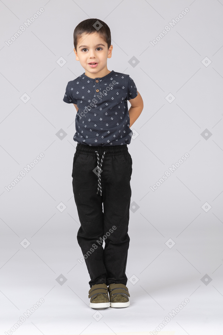 Vista frontal de un niño impresionado posando con las manos en la espalda