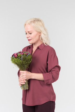 A nice-looking middle-aged blonde woman in a burgundy shirt and with a simple bouquet of flowers in her hands