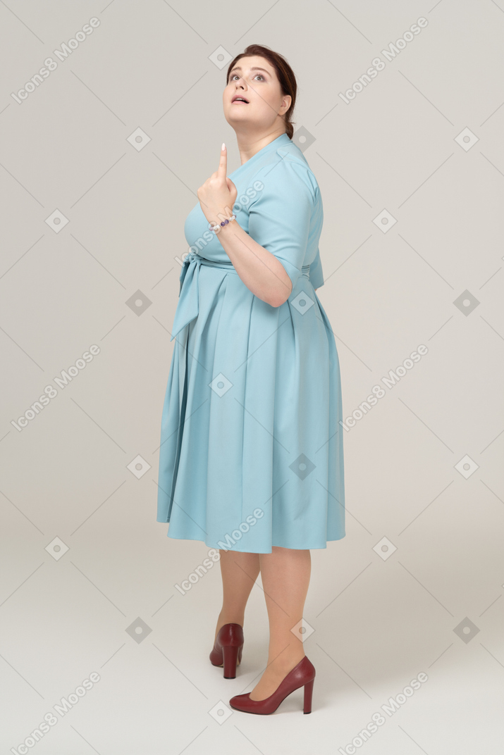 Side view of a woman in blue dress pointing up with a finger