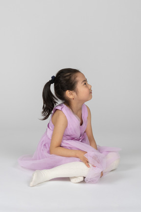 Girl in a pink dress sitting on the floor and looking up