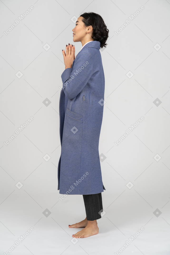 Vista laterale di una donna in cappotto blu con le mani giunte