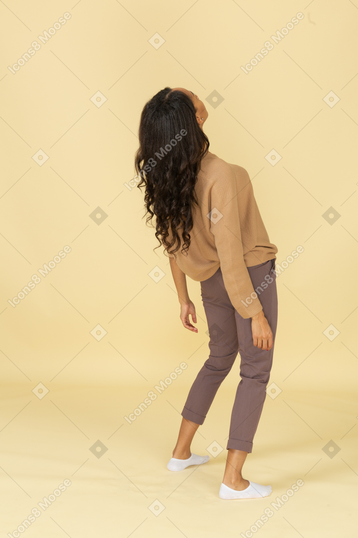Three-quarter back view of a tired dark-skinned young female leaning back