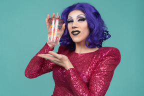 Retrato de una drag queen con vestido rosa sonriendo mientras muestra un vaso de plástico