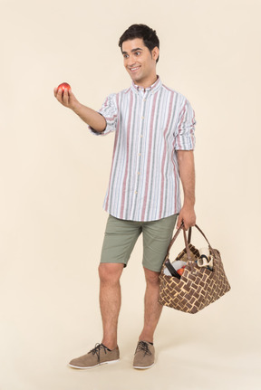 Young guy holding picnic basket and holding out a fruit