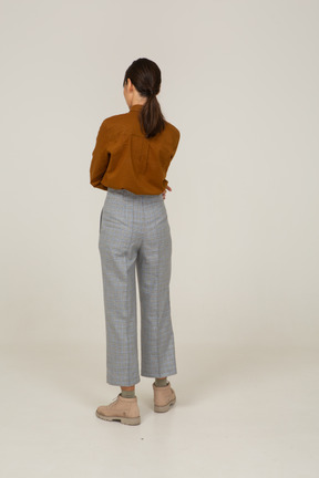 Vista posterior de tres cuartos de una mujer asiática joven pensativa en calzones y blusa