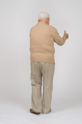 Vista trasera de un anciano con ropa informal que muestra el pulgar hacia arriba