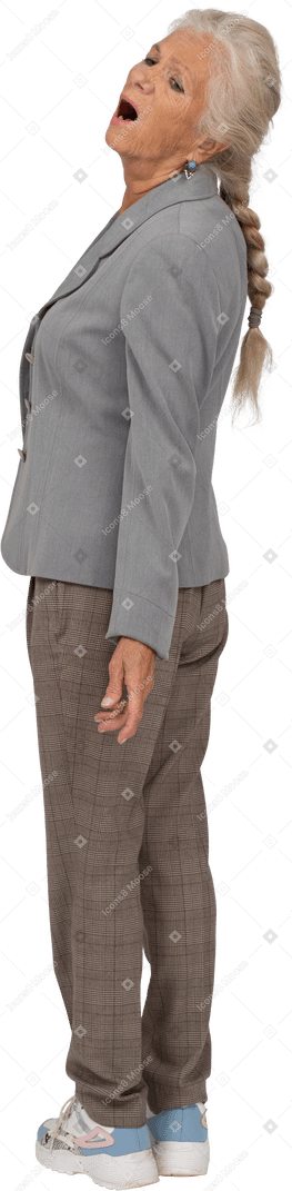Вид сбоку эмоциональной старушки в костюме, стоящей с открытым ртом