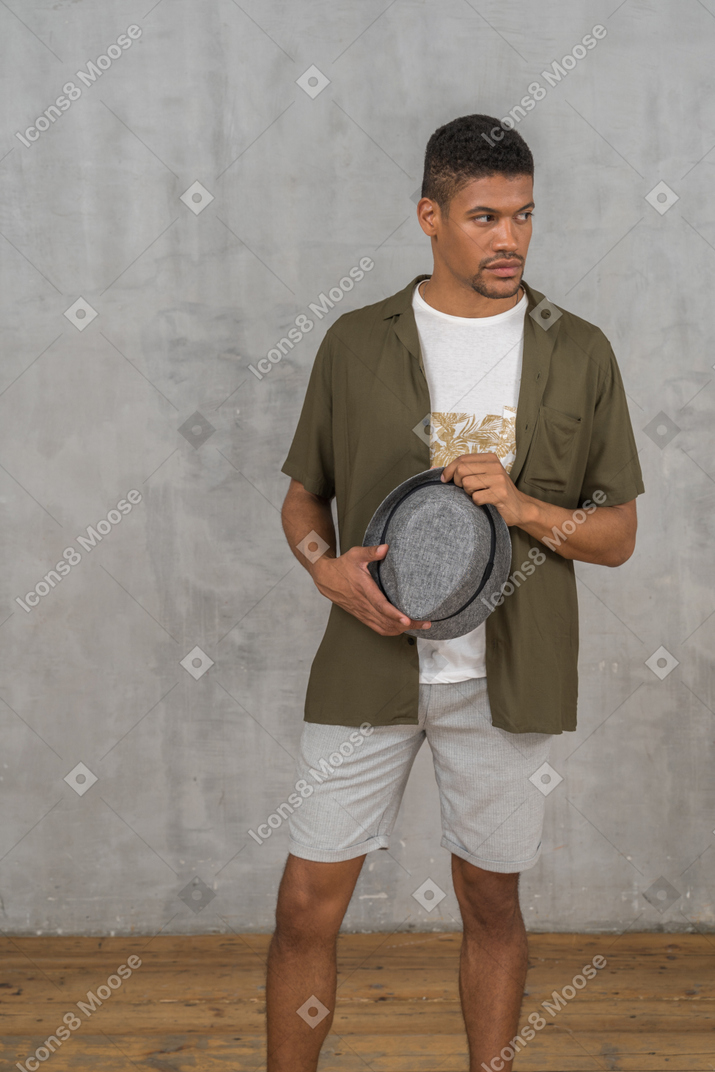 Young man looking aside while holding hat