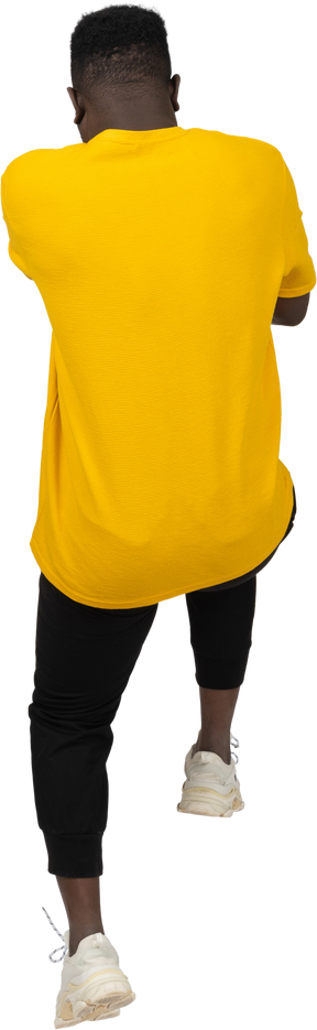 Rückansicht eines jungen dunkelhäutigen mannes im gelben t-shirt, der zurück springt