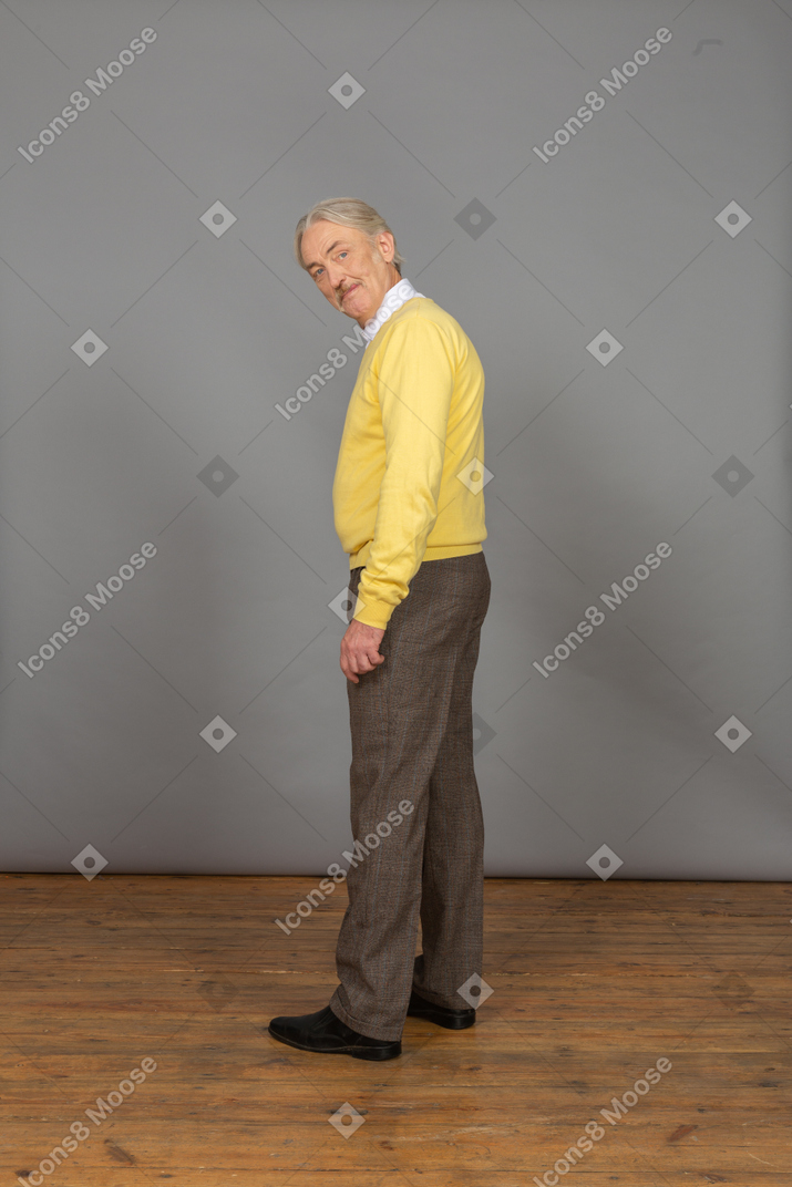 一个黄色的套衫弯下腰，看着相机的开朗老人的侧视图