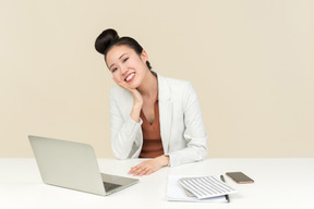 Lächelnder weiblicher asiatischer büroangestellter, der am schreibtisch sitzt