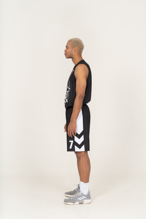 Vista lateral de un joven jugador de baloncesto masculino haciendo pucheros de pie todavía