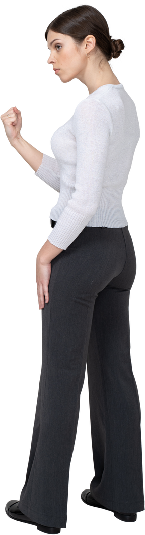 Vista posteriore di tre quarti di una giovane donna severa in abiti da ufficio che mostra il pugno