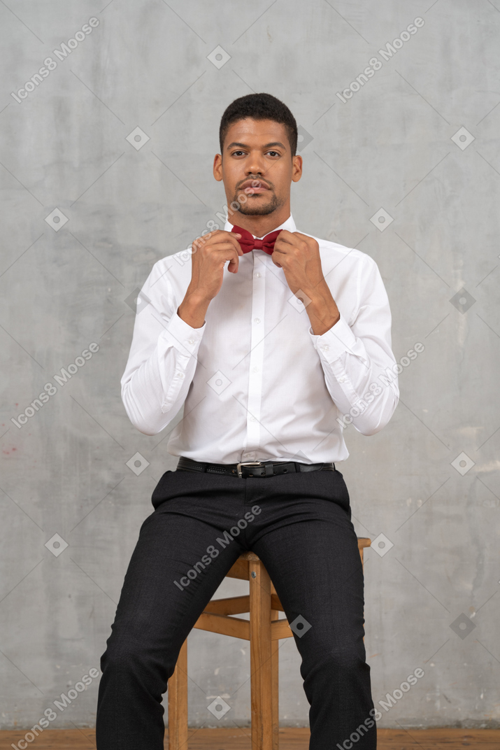 Junger mann sitzt auf einem stuhl und passt seine fliege an