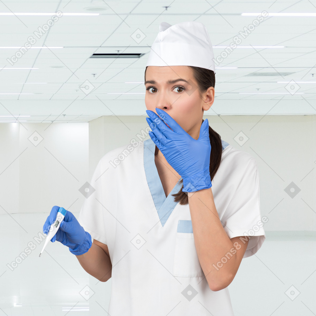 A female nurse is holding a thermometer and looking shocked