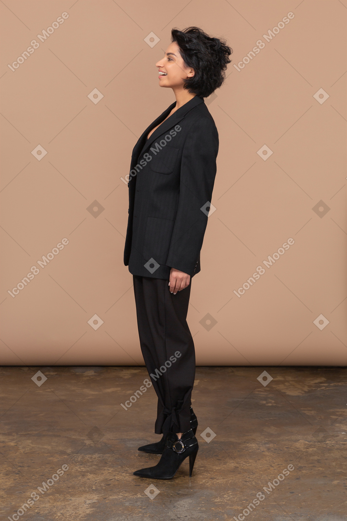 Вид сбоку удивленной улыбающейся бизнес-леди в черном костюме