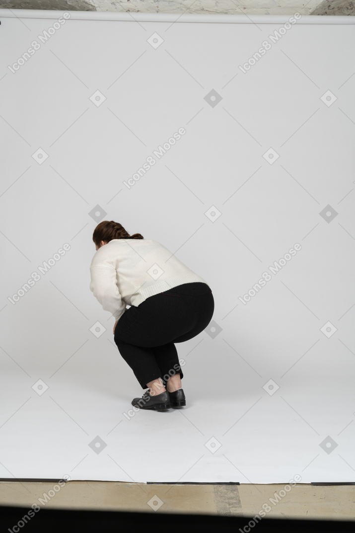 Rear view of a plump woman in casual clothes squatting