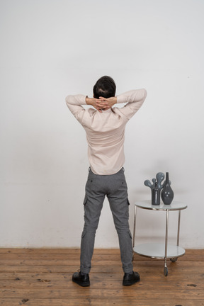 Rear view of a man in casual clothes standing with hands behind head