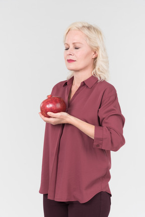 A nice-looking middle-aged blonde woman in a burgundy shirt and a pomegranate in her hand