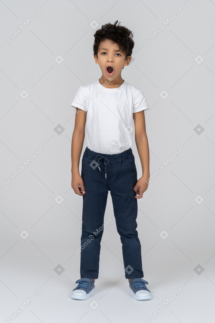 Yawning boy stands with his hands alongside body