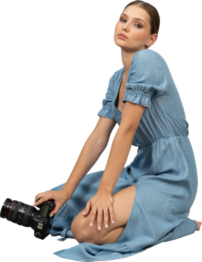 Side view of a young woman in blue dress sitting on a floor with camera